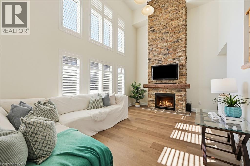 Soaring ceilings with upper windows, integrated wall-mounted fireplace with stone surround, wood mantel, and wood-finish flooring - 3198 Tim Dobbie Drive, Burlington, ON