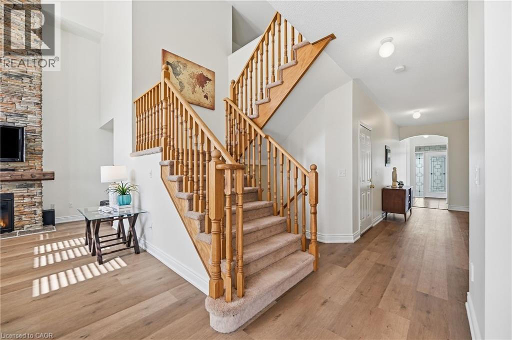 Hardwood-finish flooring, a carpeted staircase with wood banisters, a stone-clad fireplace, and a high ceiling - 3198 Tim Dobbie Drive, Burlington, ON