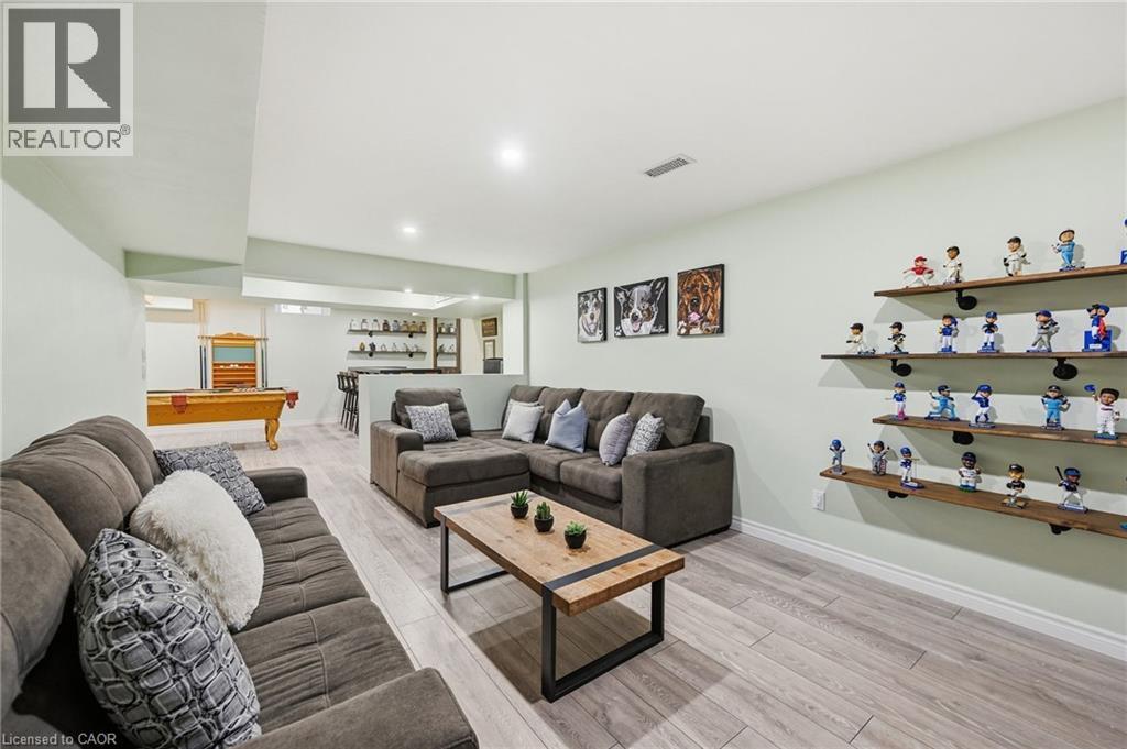 Spacious recreational room featuring wood-finish flooring, recessed lighting, built-in shelving, and a wet bar with open shelving - 3198 Tim Dobbie Drive, Burlington, ON