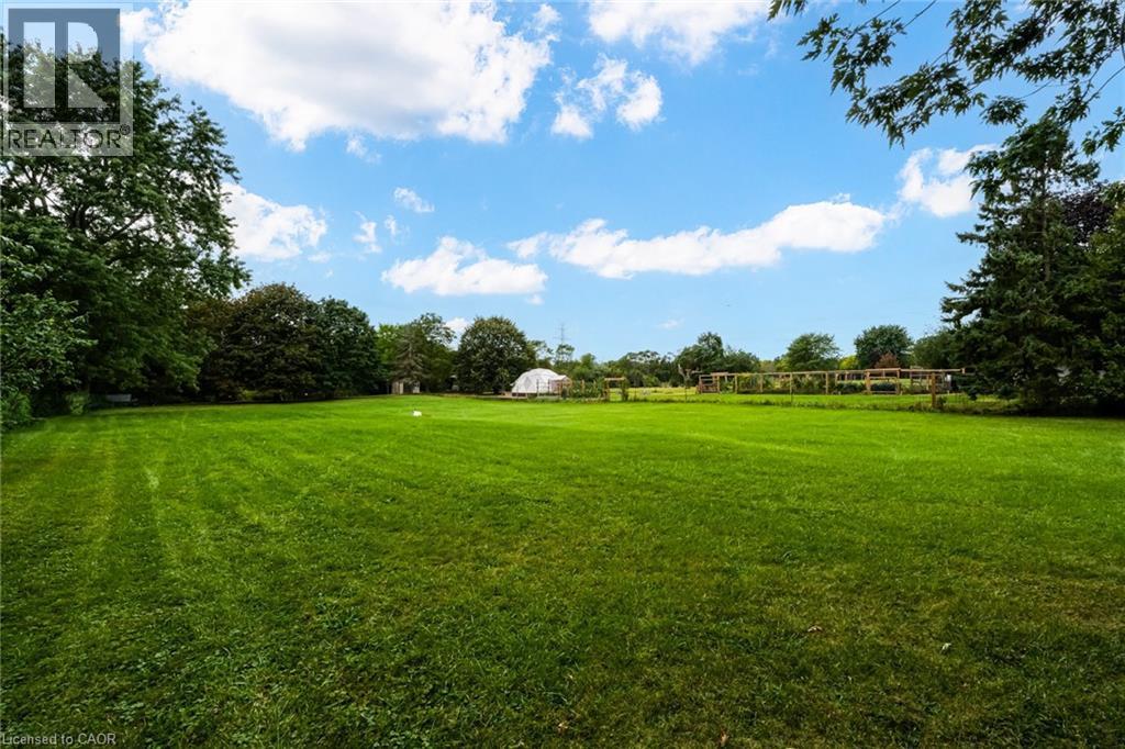 Expansive green lawn with mature trees, a distant greenhouse, and a perimeter fence - 1412 Old York Road, Burlington, ON
