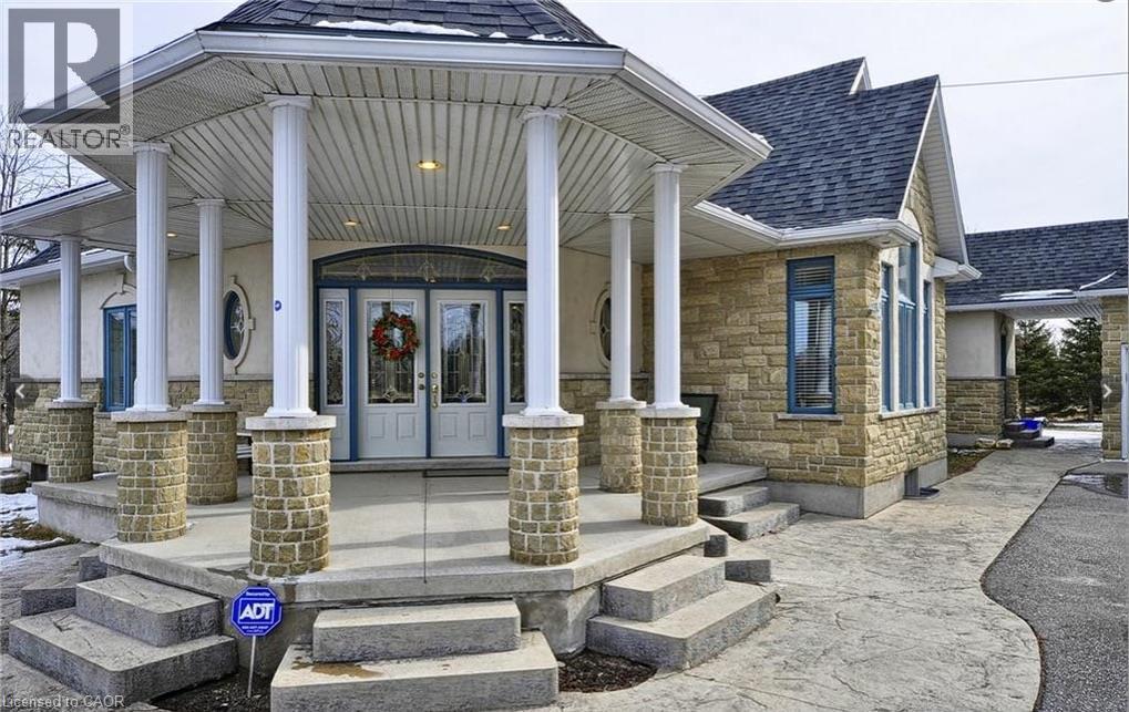Stone veneer exterior with a covered portico, multiple support columns, and an arched transom window above the double entry doors - 915 Briardean Road, Cambridge, ON