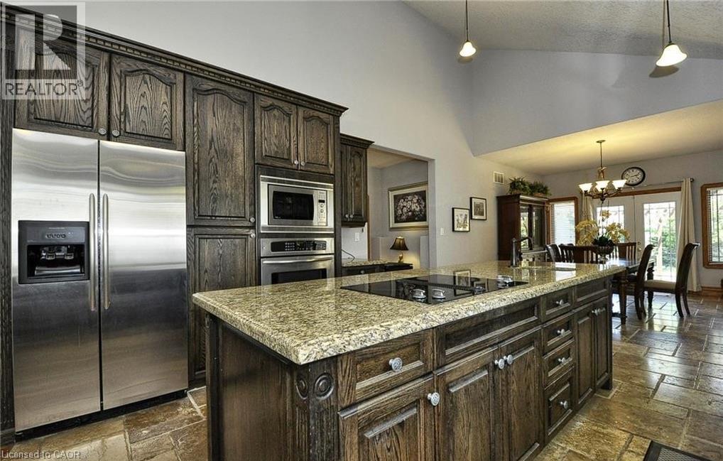 Kitchen featuring dark wood cabinetry, stainless steel appliances, a center island with a cooktop, granite countertops, and stone tile flooring - 915 Briardean Road, Cambridge, ON
