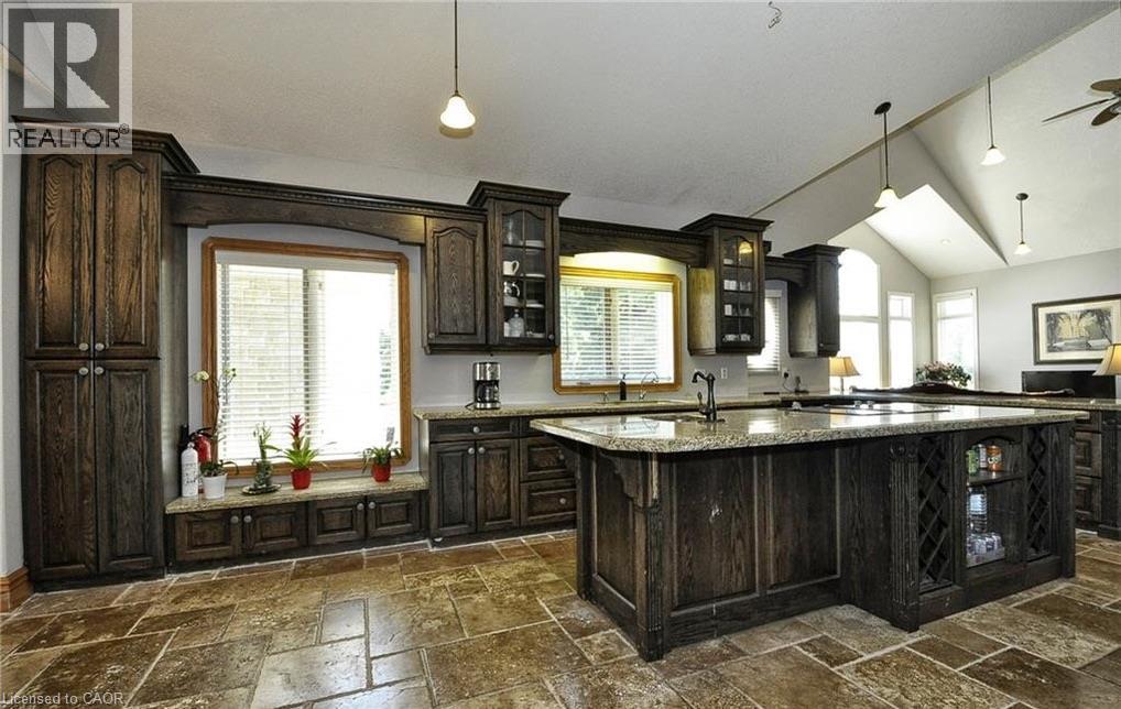 Spacious kitchen featuring dark wood cabinetry, a large kitchen island with integrated storage, light-toned countertops, and stone tile flooring - 915 Briardean Road, Cambridge, ON