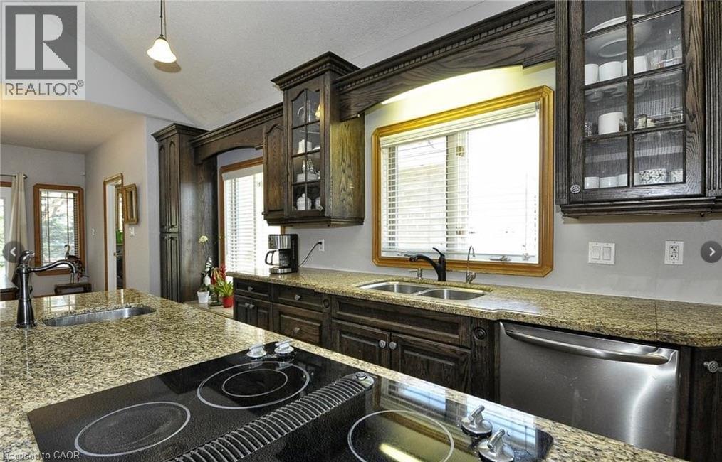 Kitchen featuring granite countertops, dark wood cabinetry, a built-in cooktop, stainless steel dishwasher, and a double basin sink - 915 Briardean Road, Cambridge, ON