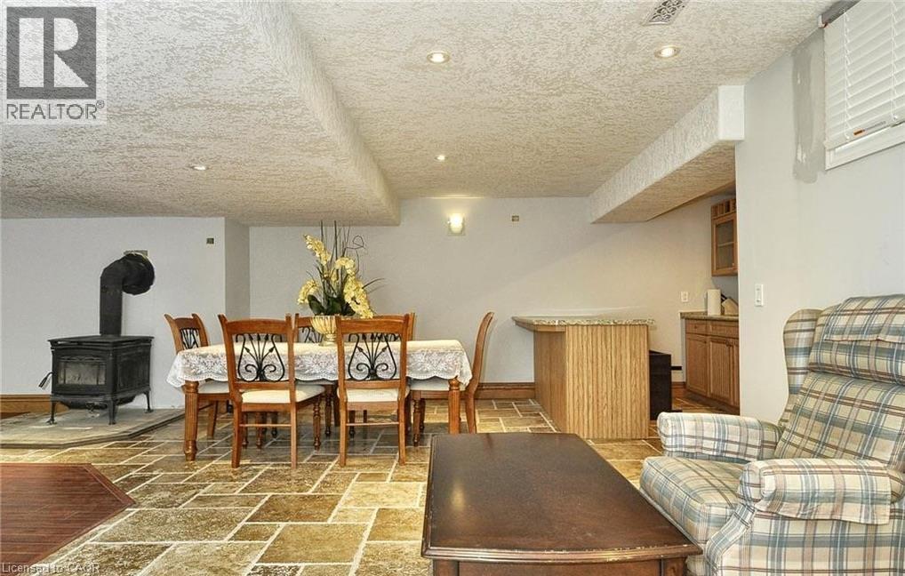 Stone tile flooring, recessed ceiling lighting, wood-burning stove, built-in wet bar with a stone-look countertop, and wood cabinetry - 915 Briardean Road, Cambridge, ON