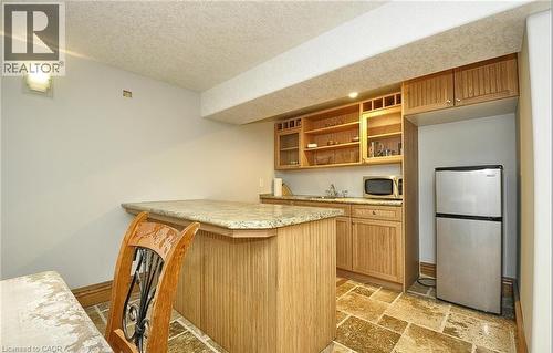 Kitchenette featuring wood cabinetry, stone-finish countertop, stainless steel refrigerator, and stone-finish flooring - 915 Briardean Road, Cambridge, ON 