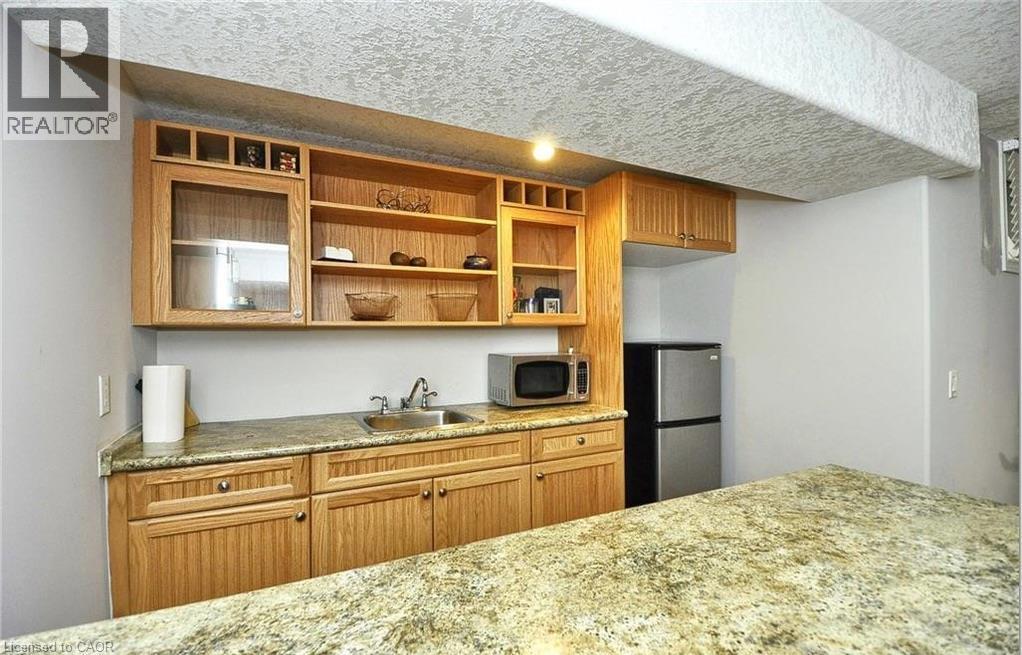 Built-in wet bar featuring a dual basin sink, light wood cabinetry, open shelving, and granite-style countertops - 915 Briardean Road, Cambridge, ON