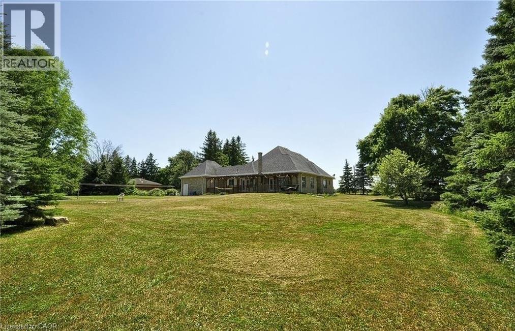 Expansive lawn with mature trees and a rear property facade featuring a covered patio - 915 Briardean Road, Cambridge, ON