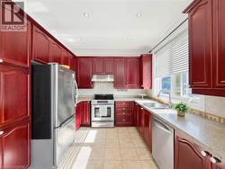 Red-toned cabinetry with crown molding, stainless steel appliances, tile flooring, light-toned countertops, and a tiled backsplash -