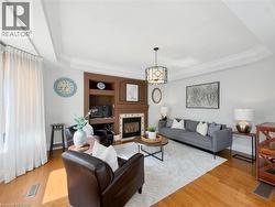 Tray ceiling with crown molding, wood-finish flooring, built-in media center, gas fireplace with tile surround, and a drum-style chandelier -