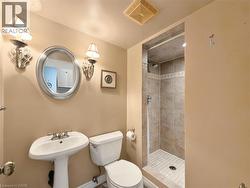 Pedestal sink with chrome fixtures, oval framed mirror, sconce lighting, tile-surround shower with mosaic accent, and tile flooring -