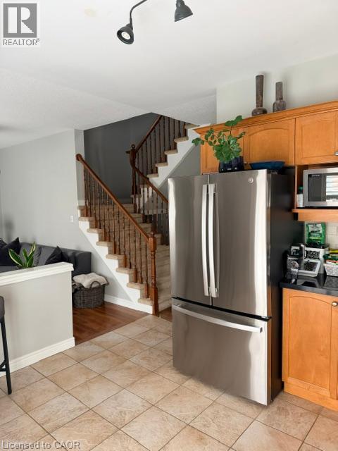 Stainless steel French door refrigerator, wood-finish cabinetry, black countertop, track lighting, and tiled flooring - 5383 Haldimand Crescent, Burlington, ON