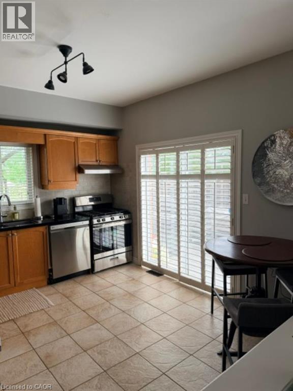 Tiled flooring, stainless steel appliances, wood cabinetry, and a sliding glass door with louvered shutters - 5383 Haldimand Crescent, Burlington, ON