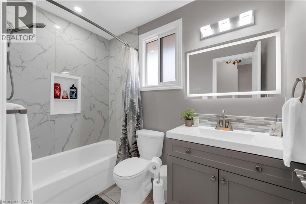 This bathroom features a white bathtub with marble-style tiled walls and a recessed shelf, alongside a toilet - 7506 Jubilee Drive, Niagara Falls, ON