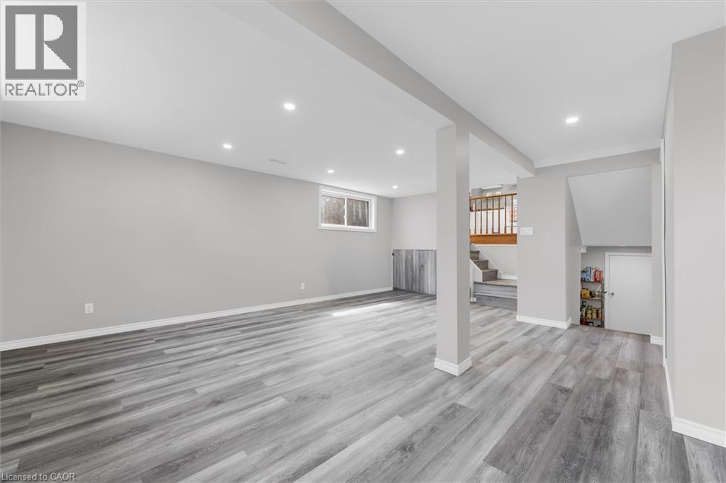 Spacious room featuring light grey walls, grey wood-style flooring, recessed lighting, and a visible window - 7506 Jubilee Drive, Niagara Falls, ON