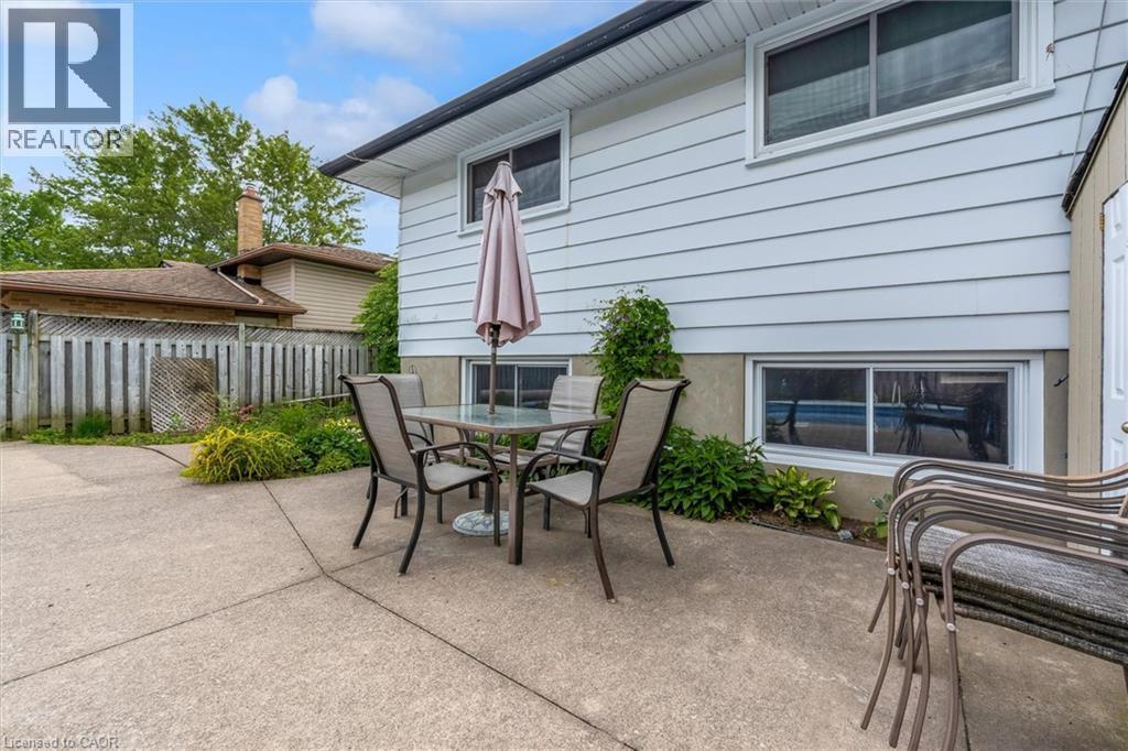 Concrete patio area featuring a white vinyl-sided exterior, upper-level casement window, lower-level sliding window, and surrounding perimeter landscaping - 7506 Jubilee Drive, Niagara Falls, ON