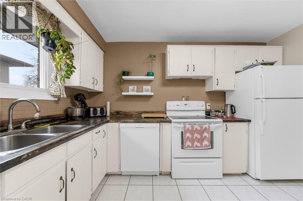 Kitchen featuring white cabinetry, a double basin stainless steel sink, and white appliances - 7506 Jubilee Drive, Niagara Falls, ON