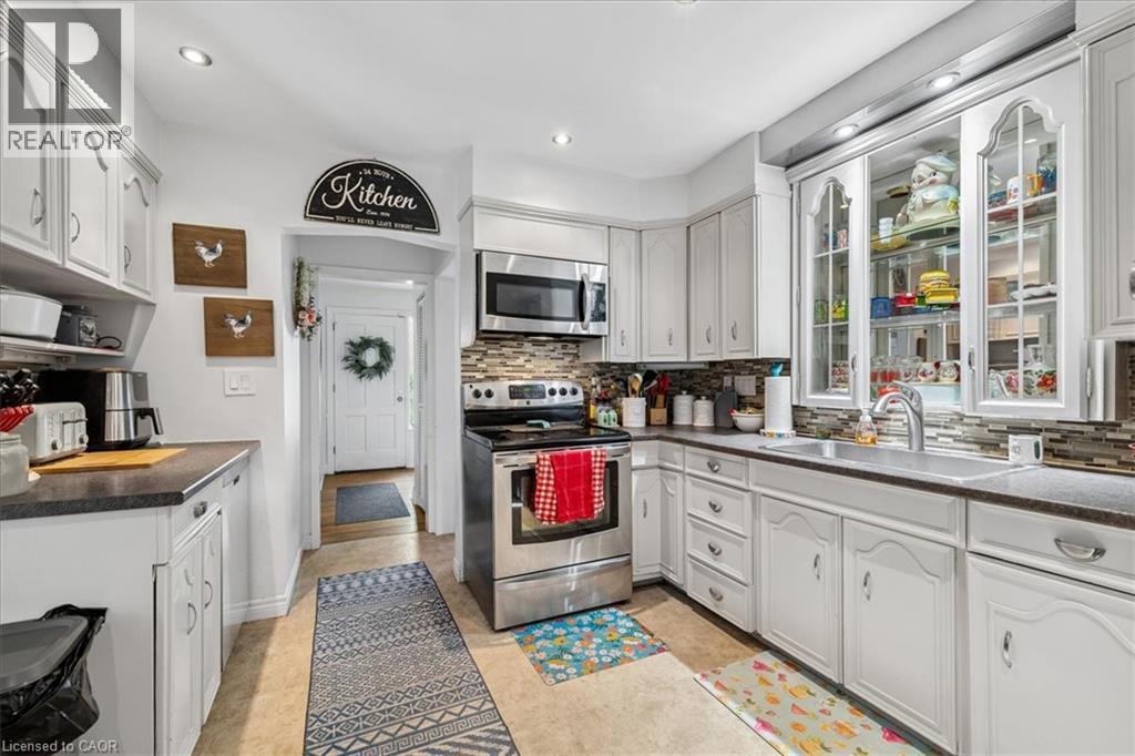 White cabinetry with decorative glass panels, stainless steel appliances, and a tiled backsplash - 80 Maclennan Avenue, Hamilton, ON