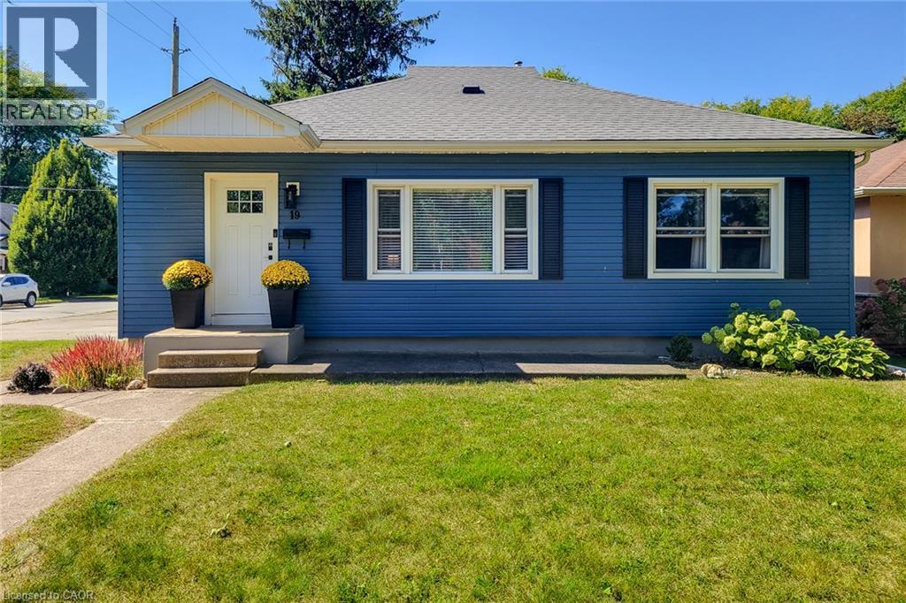 Blue horizontal siding exterior with a contrasting white front door, a gabled entry overhang, and white-framed windows with dark shutters - 19 Thorndale Avenue, St. Catharines, ON