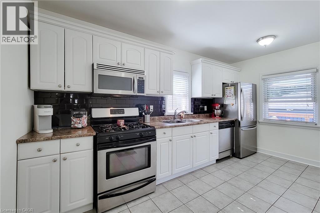 White cabinetry, stainless steel appliances, dark subway tile backsplash, granite-style countertops, and tile flooring - 19 Thorndale Avenue, St. Catharines, ON
