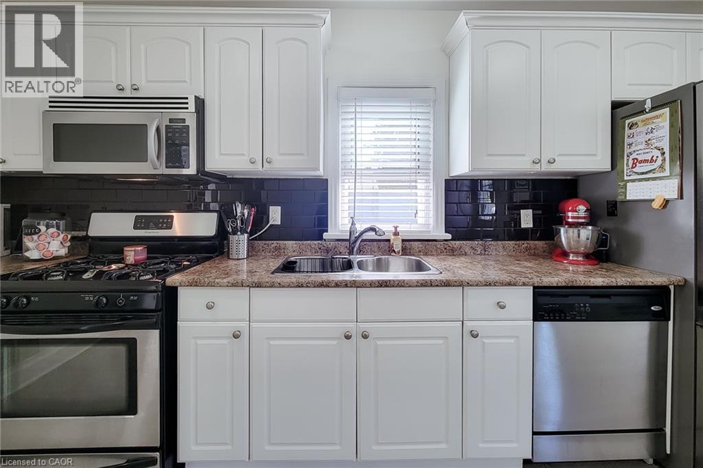 White cabinetry, dark subway tile backsplash, stainless steel appliances, double basin sink, and wood-finish countertops - 19 Thorndale Avenue, St. Catharines, ON