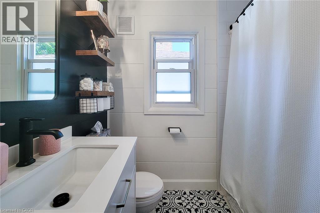 Modern bathroom featuring shiplap walls, a vanity with an integrated sink, a dark accent wall with floating wood shelves, and patterned floor tile - 19 Thorndale Avenue, St. Catharines, ON
