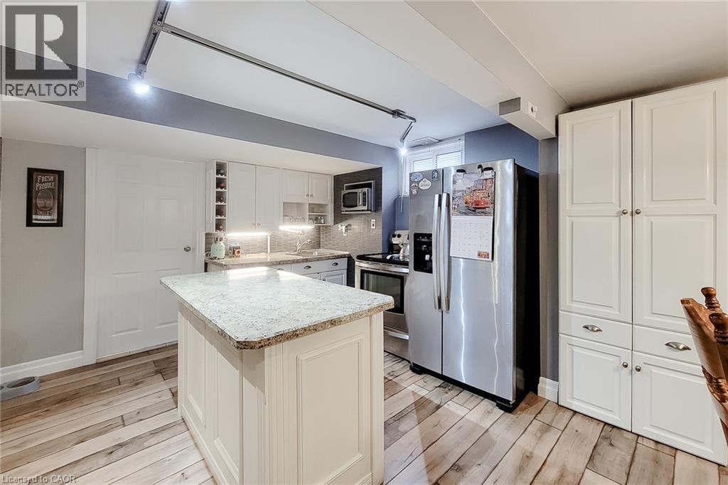 Kitchen featuring wood-finish flooring, an island with a light-toned countertop, white cabinetry with silver hardware, a stainless steel refrigerator, and track lighting - 19 Thorndale Avenue, St. Catharines, ON
