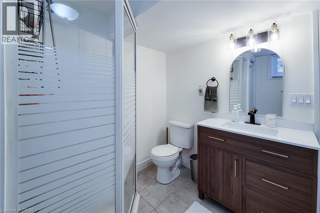 Frosted glass shower enclosure, wood-finish vanity with drawer storage, white countertop with integrated sink, black wall-mounted faucet, and arched mirror - 19 Thorndale Avenue, St. Catharines, ON