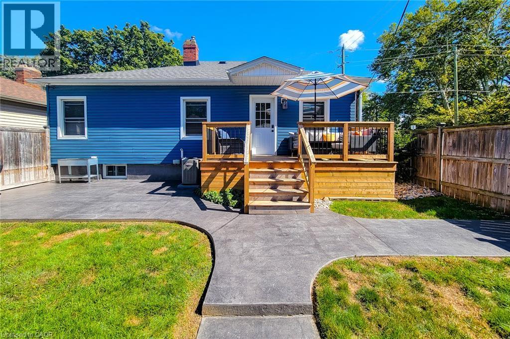 Blue siding exterior with a wood deck featuring black railing, a wood privacy fence, and a concrete patio - 19 Thorndale Avenue, St. Catharines, ON