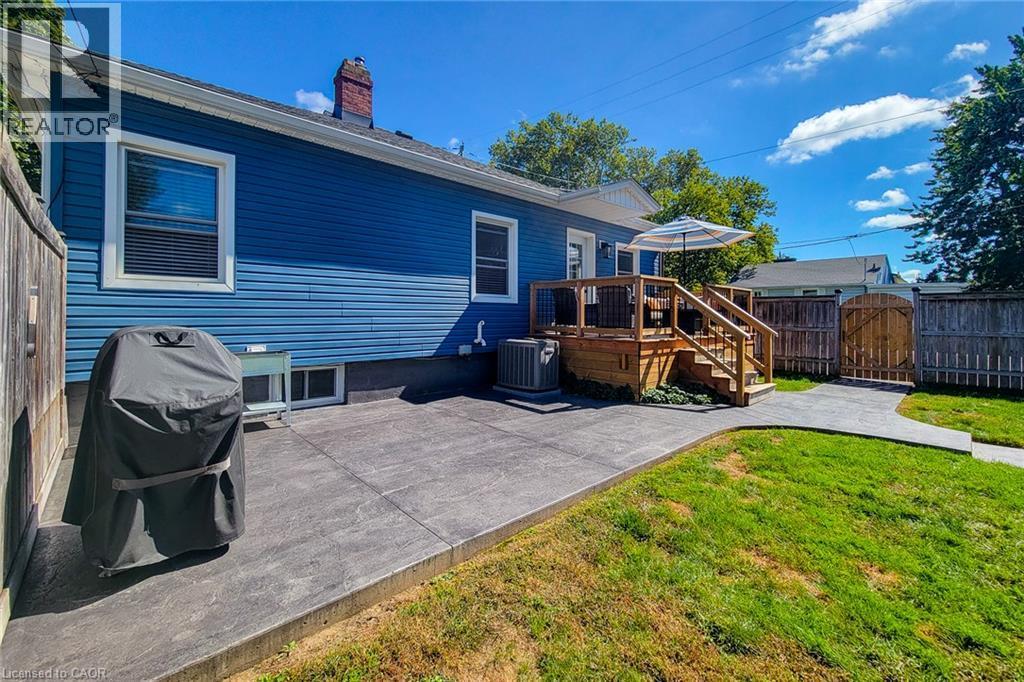 Expansive backyard featuring a manicured lawn, a wooden deck with railing, and a patterned concrete patio - 19 Thorndale Avenue, St. Catharines, ON