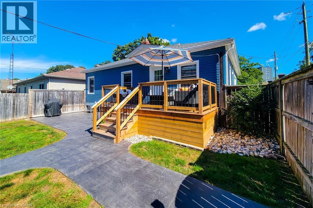Rear exterior featuring a wood deck with stairs, blue siding, stamped concrete patio, and a wood fence enclosure - 19 Thorndale Avenue, St. Catharines, ON