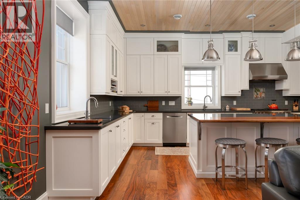 White cabinetry, dark countertops, stainless steel appliances, wood-finish flooring, and a wood-panelled ceiling - 23 Market Street W, Port Dover, ON