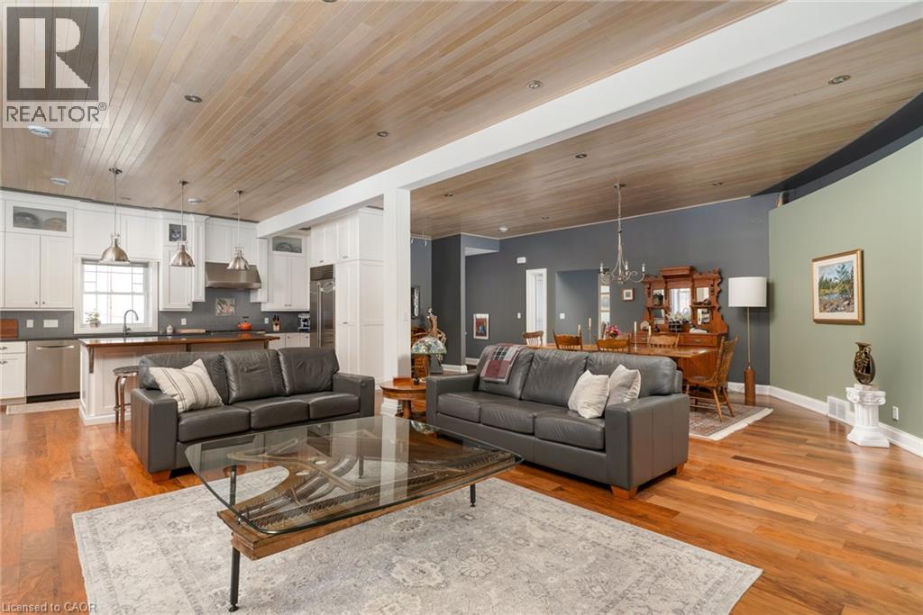 Open-concept living area with hardwood flooring, a wood-paneled ceiling, recessed lighting, and a kitchen featuring white cabinetry and stainless steel appliances - 23 Market Street W, Port Dover, ON