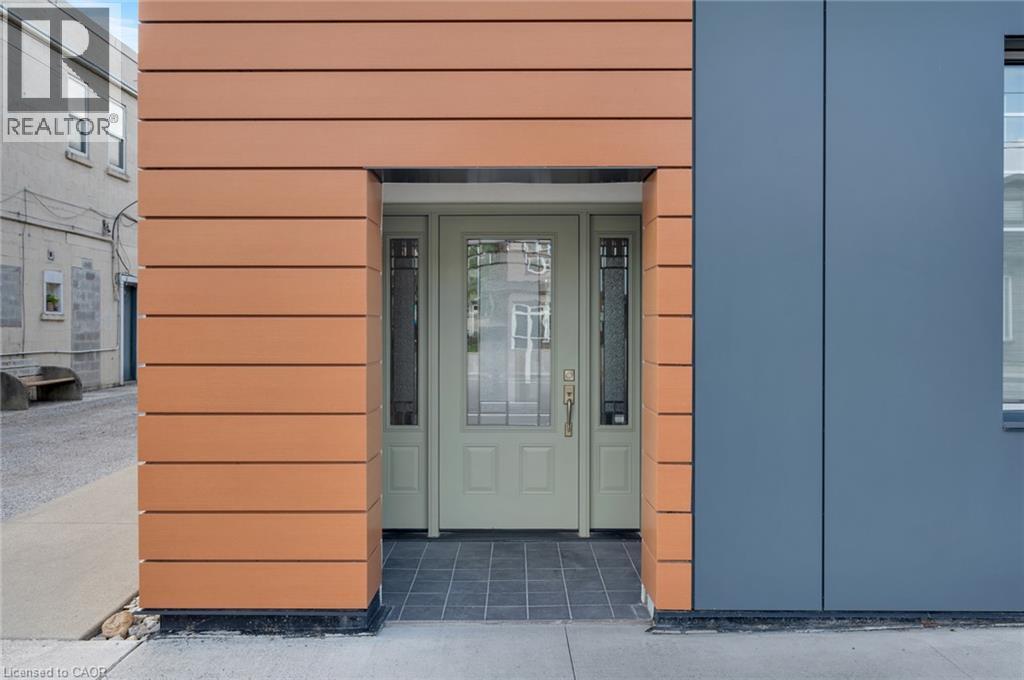 Entryway featuring a light green door with decorative glass inserts, framed by contemporary horizontal wood-finish siding and sleek gray paneling - 23 Market Street W, Port Dover, ON