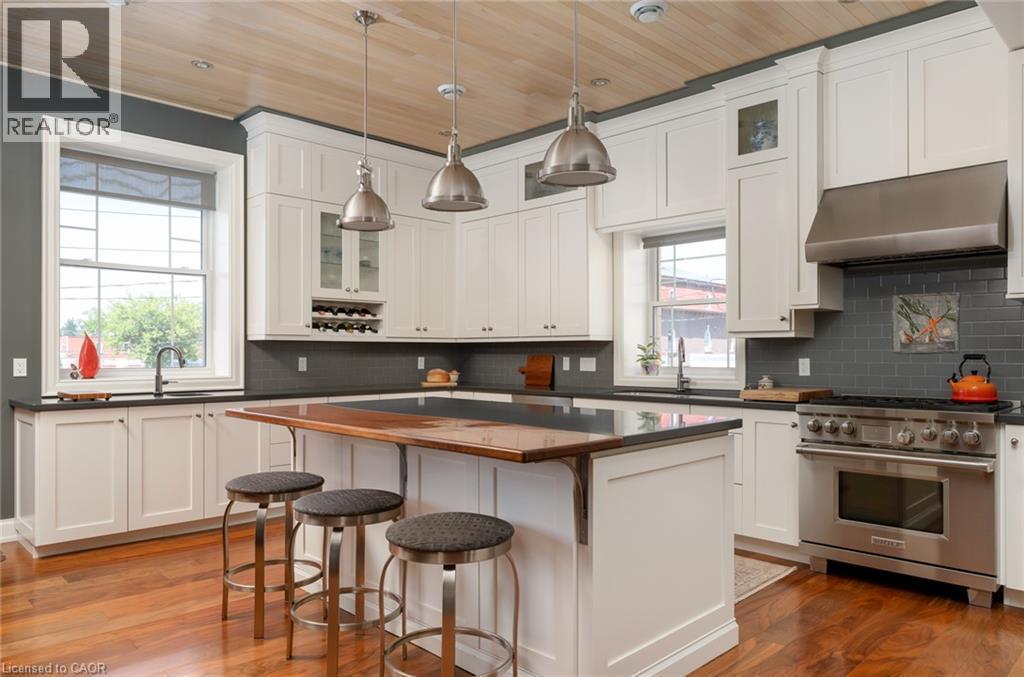 White shaker cabinetry with dark countertops, stainless steel appliances, wood-finish flooring, a wood-paneled ceiling, and a built-in wine rack - 23 Market Street W, Port Dover, ON