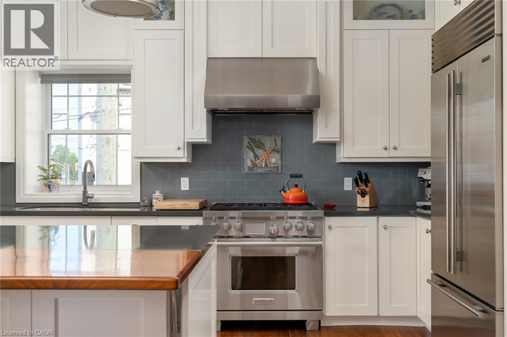 White shaker-style cabinetry, stainless steel appliances, dark subway tile backsplash, and a large window above the sink - 23 Market Street W, Port Dover, ON