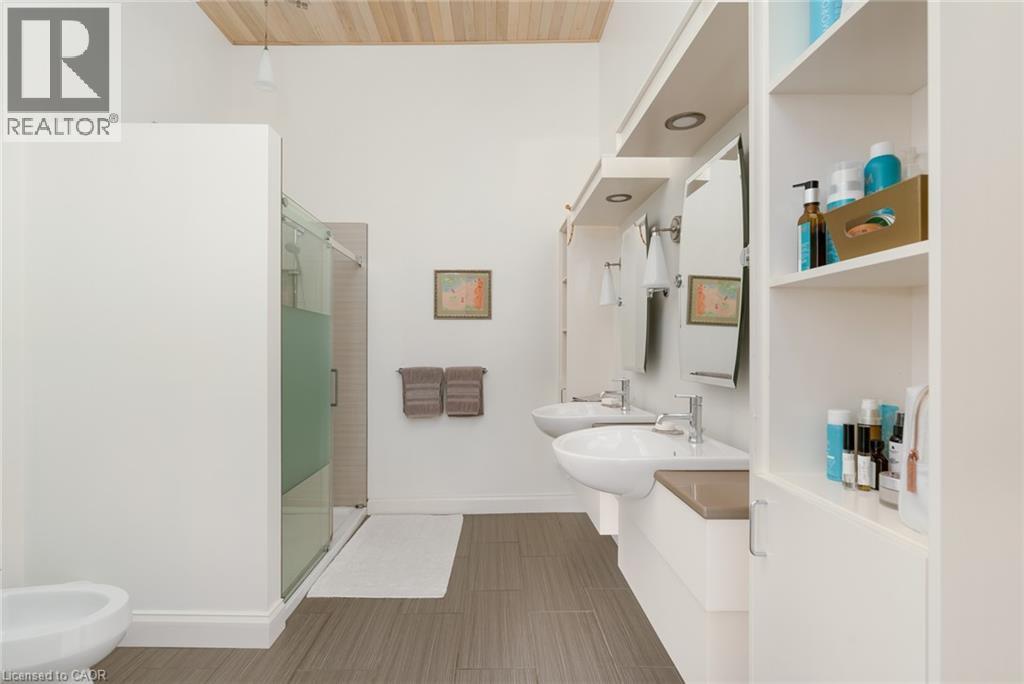 Dual floating vanities with integrated vessel sinks, extensive built-in shelving, glass-enclosed shower, and wood-finish ceiling - 23 Market Street W, Port Dover, ON