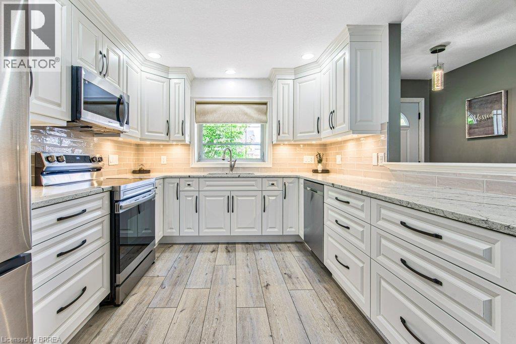 White cabinetry with black hardware, stainless steel appliances, light-toned wood-finish flooring, light-colored countertops, and an undermount sink - 423 Poldon Drive, Norwich, ON
