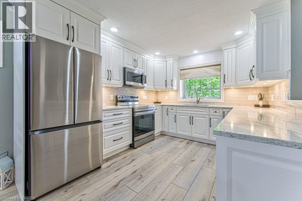 White cabinetry, stainless steel appliances, light wood-finish flooring, light-toned countertops, and a tiled backsplash - 423 Poldon Drive, Norwich, ON