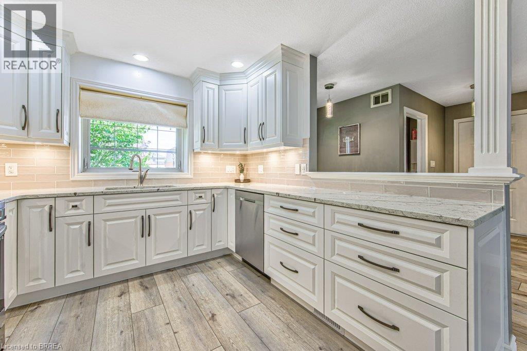 White cabinetry with dark hardware, undermount sink with a gooseneck faucet, light-toned tile backsplash, recessed lighting, and wood-finish flooring - 423 Poldon Drive, Norwich, ON