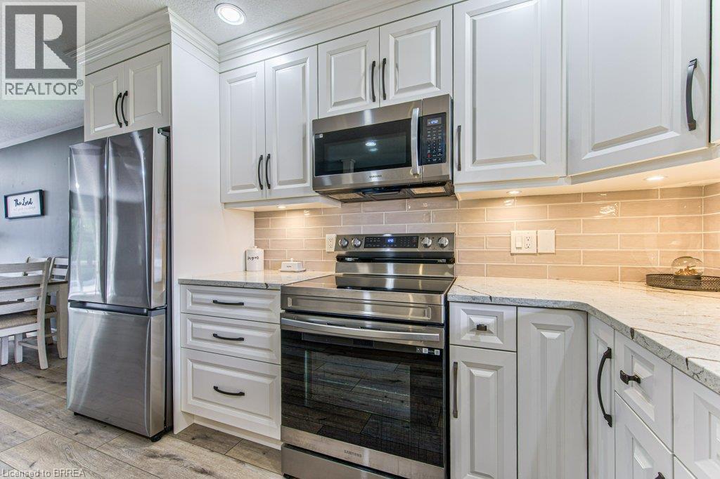 White shaker-style cabinetry with dark hardware, stainless steel appliances, light-toned subway tile backsplash, light-colored countertops, and wood-finish flooring - 423 Poldon Drive, Norwich, ON