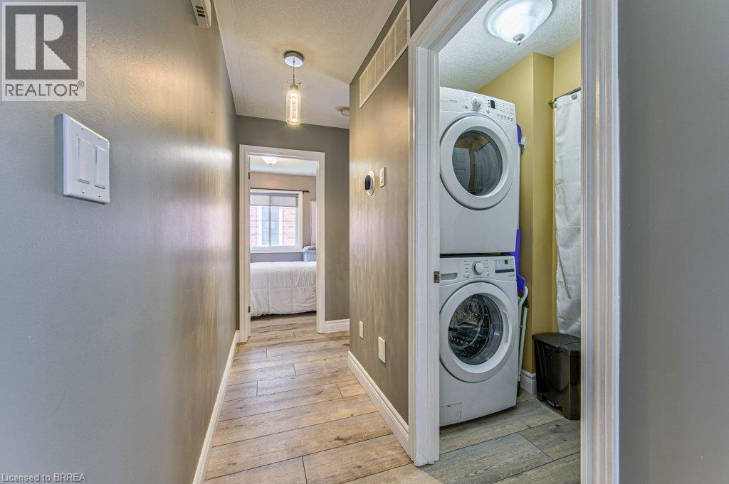 Hallway featuring wood-finish flooring, a pendant light fixture, and a laundry closet with stacked appliances - 423 Poldon Drive, Norwich, ON