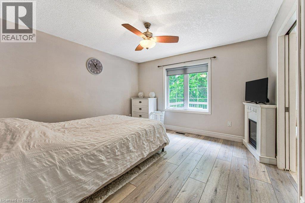 Wood-finish flooring, ceiling fan with integrated lighting, a window with a white frame, and a decorative fireplace - 423 Poldon Drive, Norwich, ON