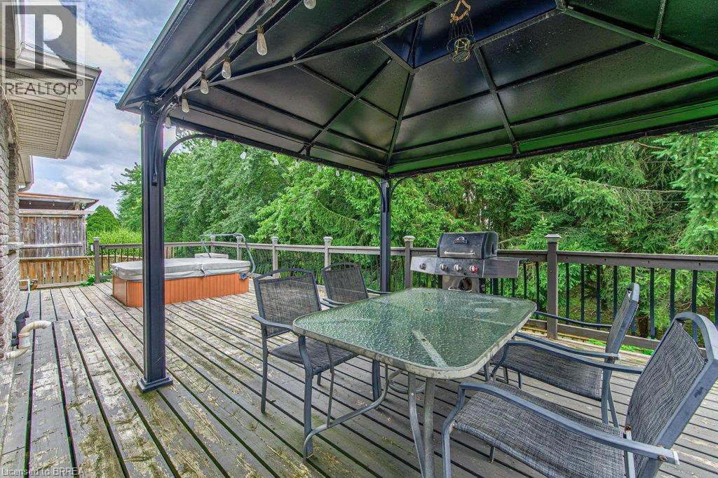 Expansive outdoor deck featuring a hot tub, gazebo, and surrounding mature trees - 423 Poldon Drive, Norwich, ON