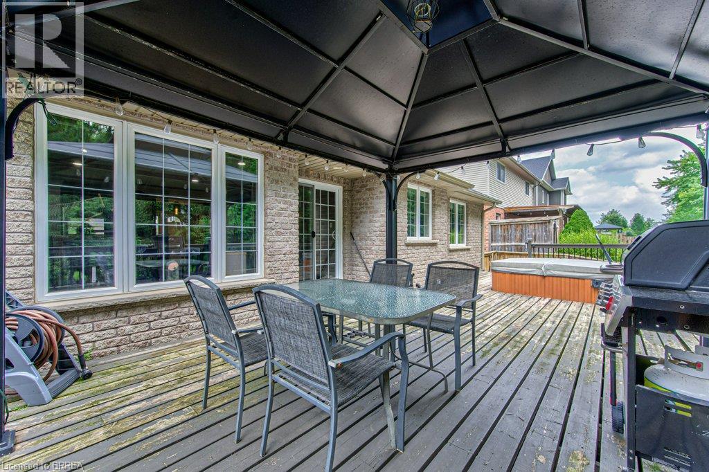 Expansive outdoor deck with a hot tub and a black metal gazebo, complemented by a brick exterior with multiple windows and a sliding glass door - 423 Poldon Drive, Norwich, ON