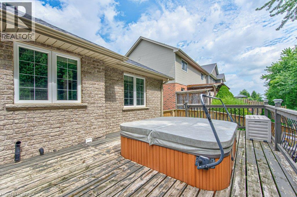Exterior brick facade with multiple windows, leading to a wooden deck featuring a built-in spa - 423 Poldon Drive, Norwich, ON