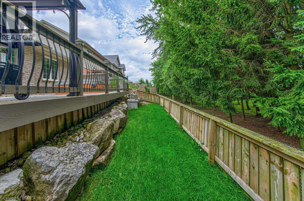 Expansive green space featuring a wood fence, mature evergreen trees, and a rock garden bordering the deck - 423 Poldon Drive, Norwich, ON