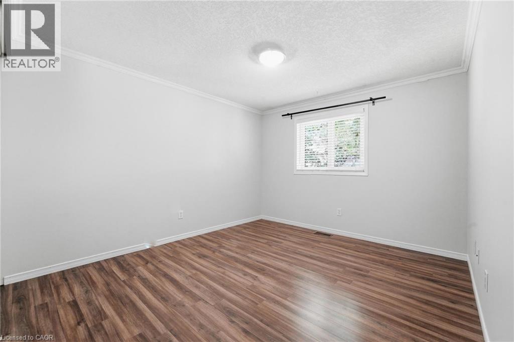 Wood-finish flooring, white painted walls, crown molding, and a single window with blinds - 449 Exmoor Street, Waterloo, ON