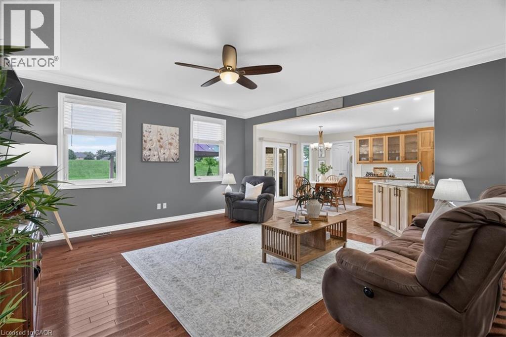 Wood-finish flooring, ceiling fan with integrated lighting, multiple windows, and a clear line of sight to the adjacent kitchen and dining area - 515 Woodward Drive, Mount Brydges, ON