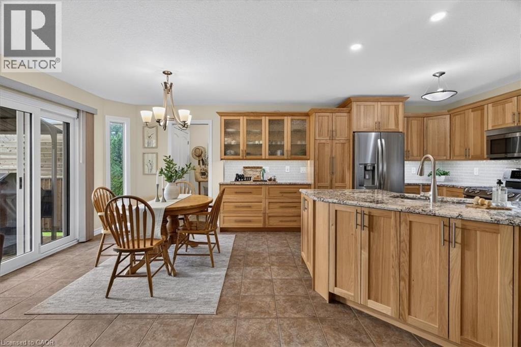 Expansive kitchen featuring wood cabinetry, stainless steel appliances, a large island with a stone countertop, and tile flooring - 515 Woodward Drive, Mount Brydges, ON